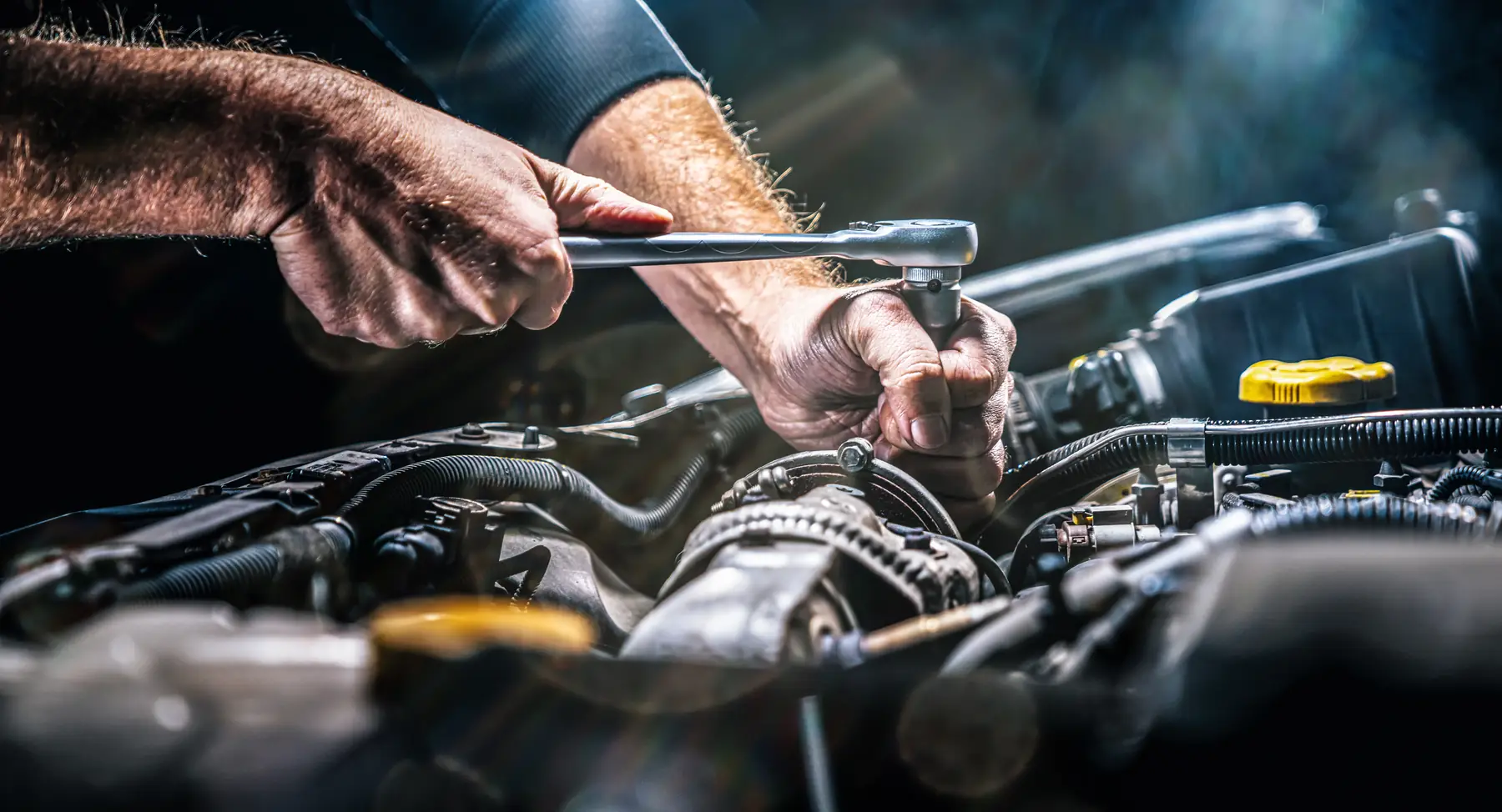 Mechanikerhände mit Ratsche an einem Motor in der Werkstatt